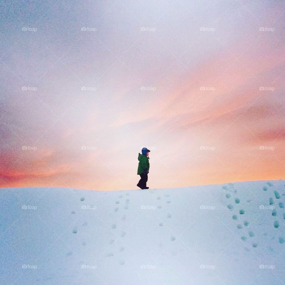 Boy walking on pile of snow in pink sunset 