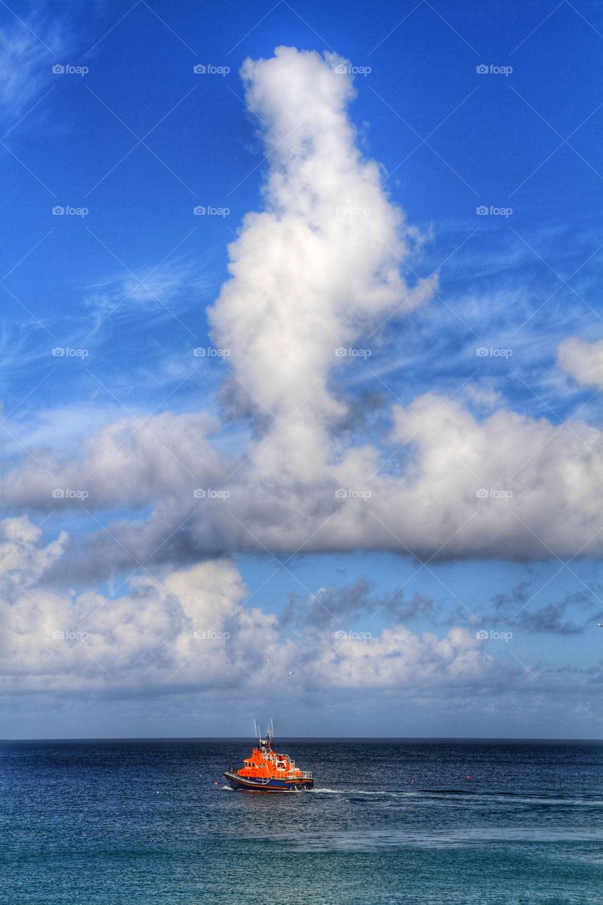 RNLI Lifeboat At Sea. An RNLI Lifeboat on its way out to sea on a bright day with interesting cloud formations above.