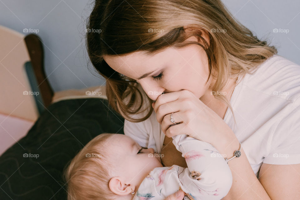 Young mum kissing her baby, breastfeeding. At home.