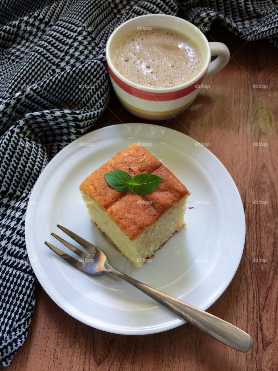 A cup of milk tea with a piece of butter cake isolated on wooden table .