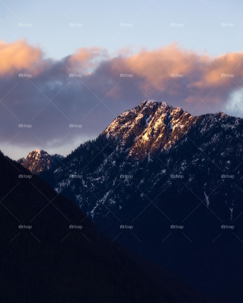 The last bit of golden sunlight illuminating on the tip of a tall majestic mountain top. British Columbia canada