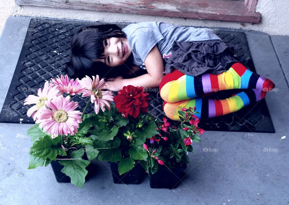 child laying on doormat behind flowers