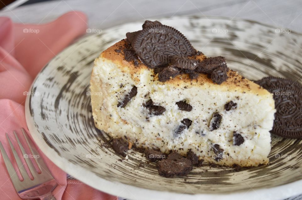 Oreo cookie cheesecake on a high contrasting plate and a pink napkins and fork