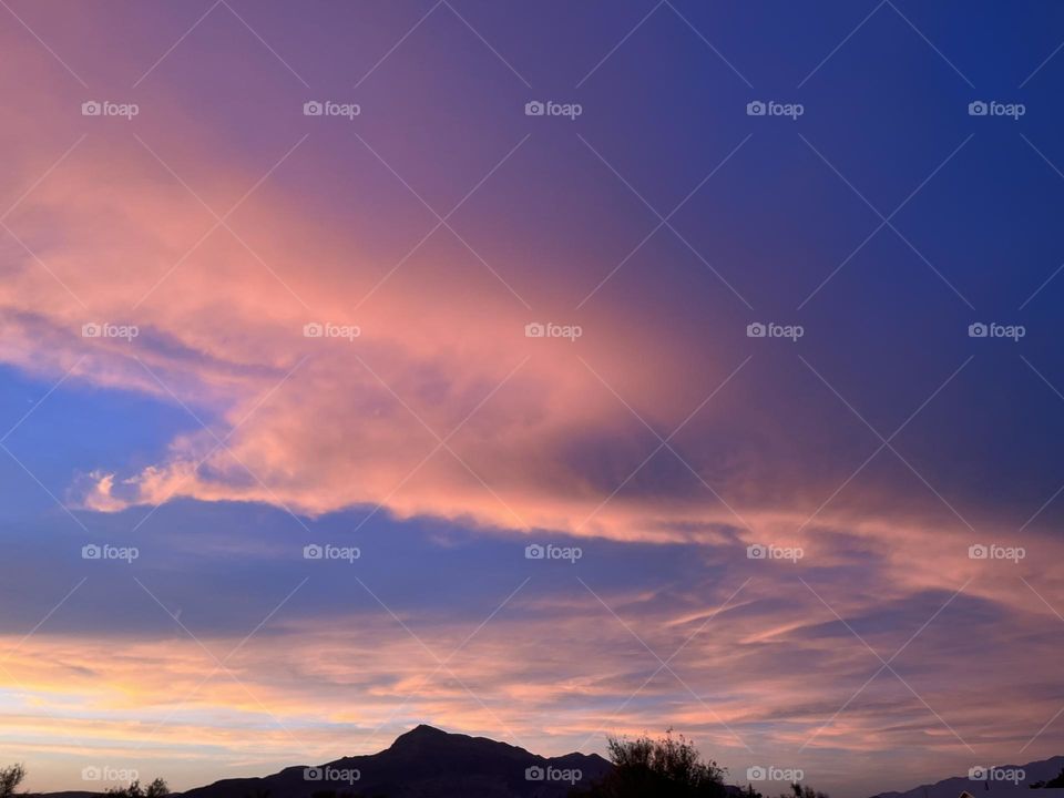 A photo of a mountain with pink clouds above. 