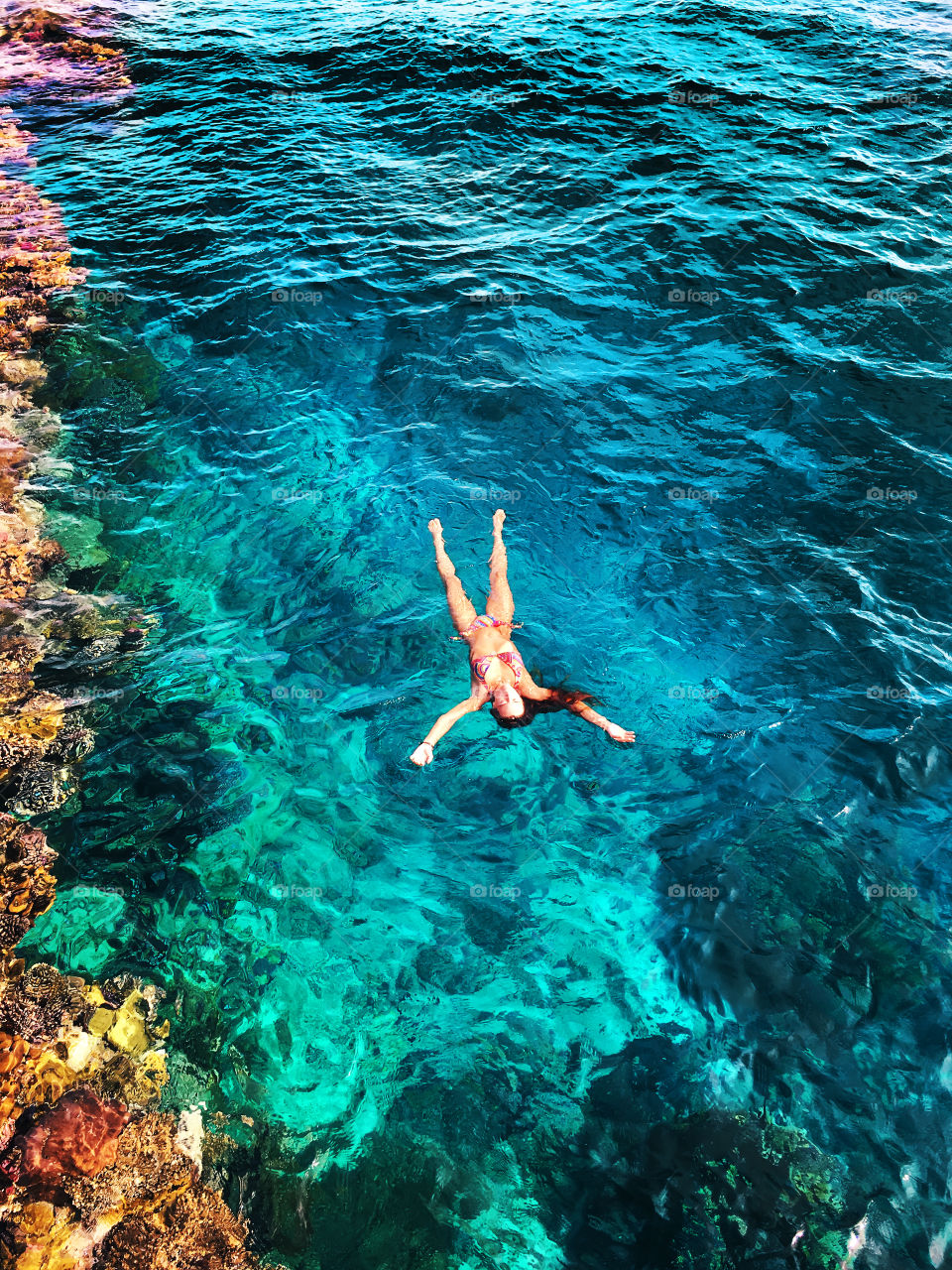 Overhead view of a young woman swimming in the blue coral sea water 