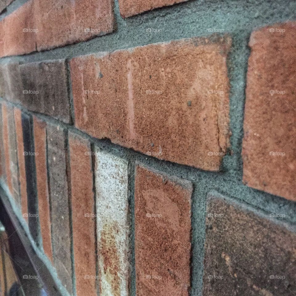 A brick wall as seen from an angle. The brick is close and brownish red. The oblique angle gives a good sense of the texture of the wall.