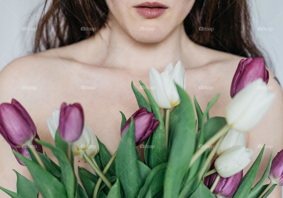 Woman holding white and purple tulips, close to her body in celebration of women day.