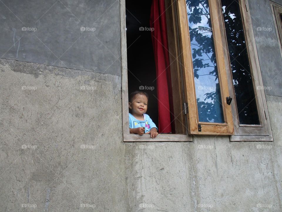 Smiling cute little girl under five years old on the window of the house