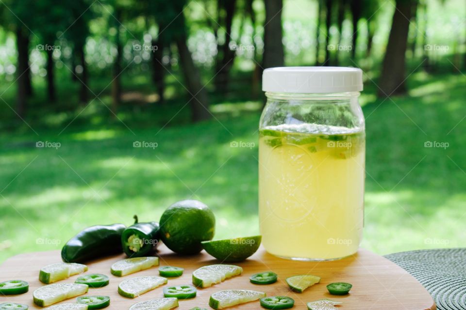 Refeshing lime-and-jalepeño-flavored kombucha, rebottled in a quart-size mason jar for a second ferment, with slices of lime and jalepeño on a bamboo cutting board, against a blurred outdoor background in summer