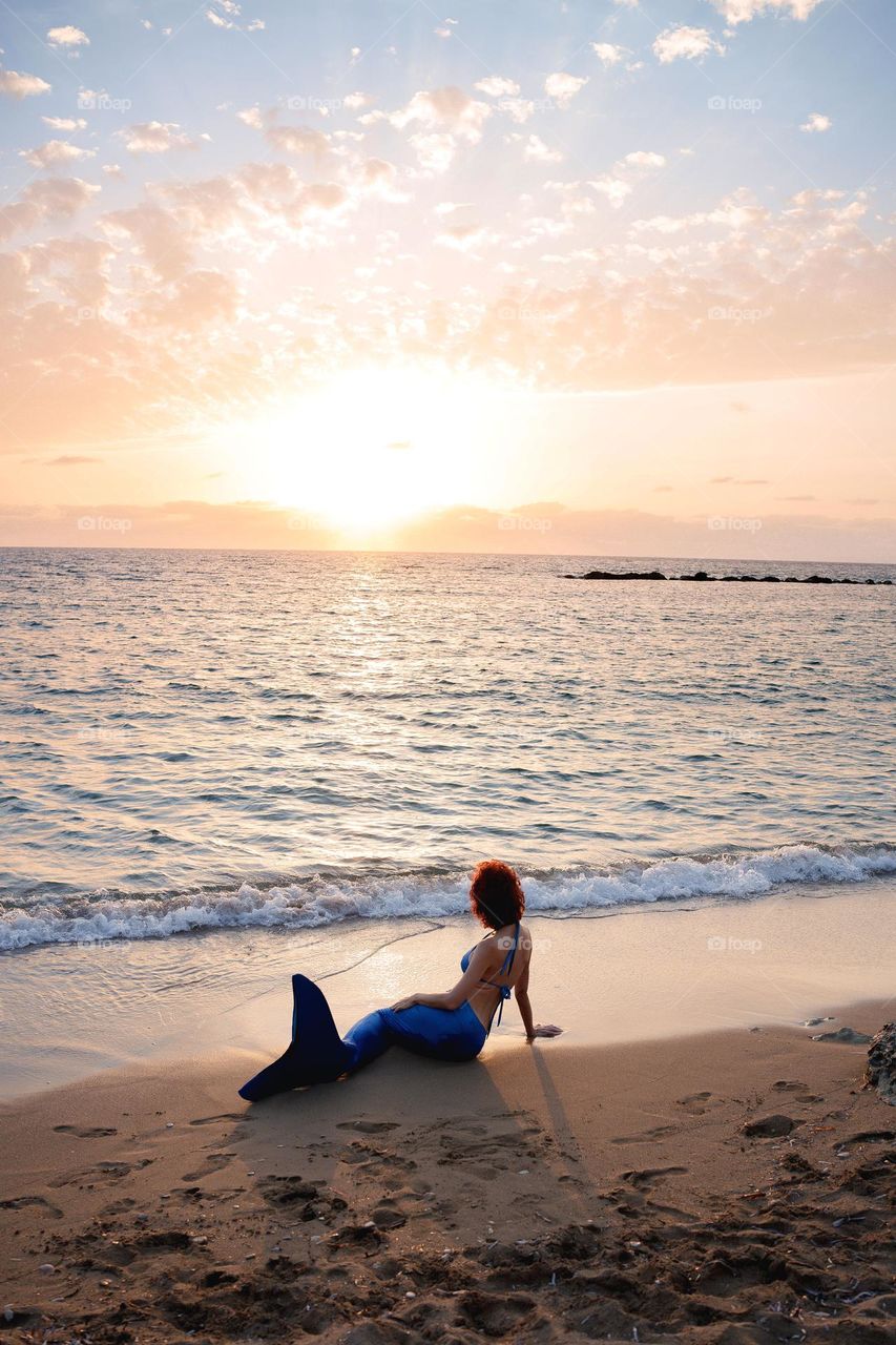 Red hair woman in mermaid costume sitting on the beach. Cosplay photo