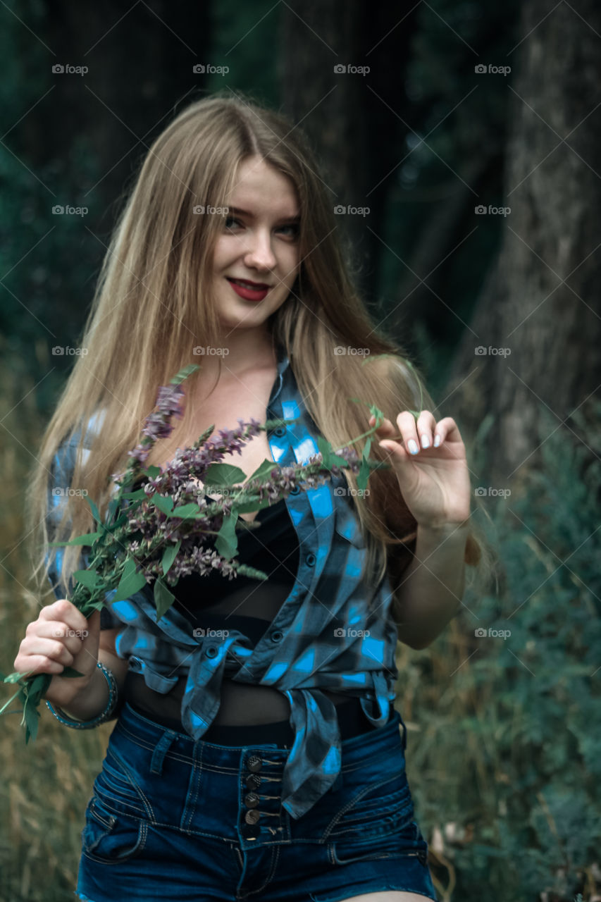 A girl with blond hair in a plaid shirt and short denim shorts on a background of trees and nature Girl, woman, man, people, blonde, blonde hair, checkered shirt, shorts shorts, denim shorts, forest nature, trees, grass, feelings, emotions tenderness, love, lifestyle, lifestyle, recreation