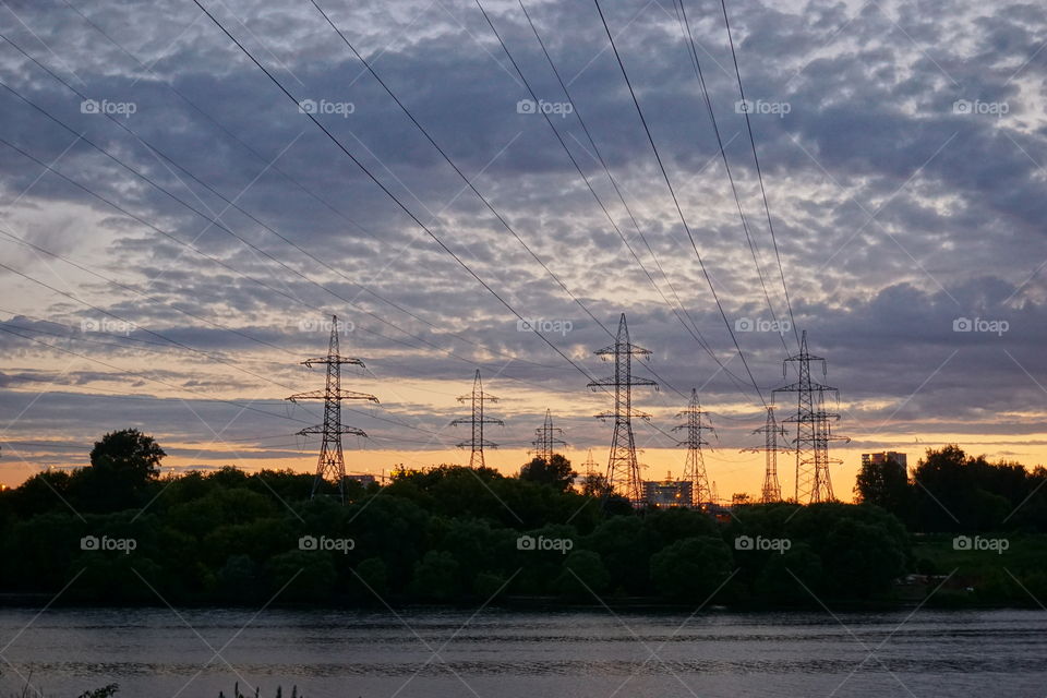 wired sunset. electricity transfer towers in front of cloudy sunset