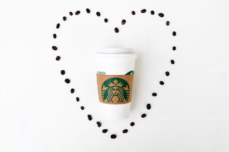 Starbucks coffee cup laid out on a white table with coffee beans surrounding it in the shape of a heart