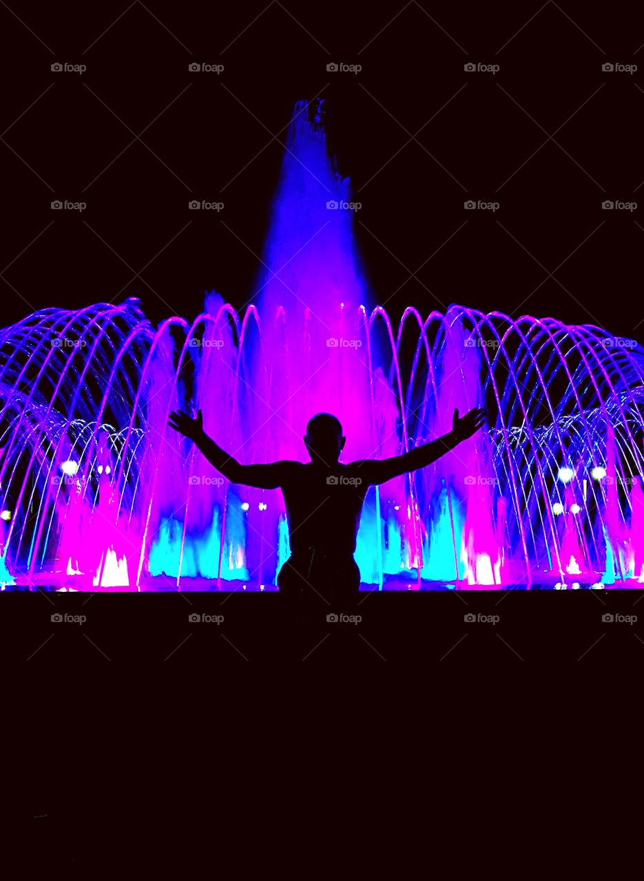 Красивый фонтан переливающийся разными цветами. Силуэт мужчины на фоне яркого фонтана.