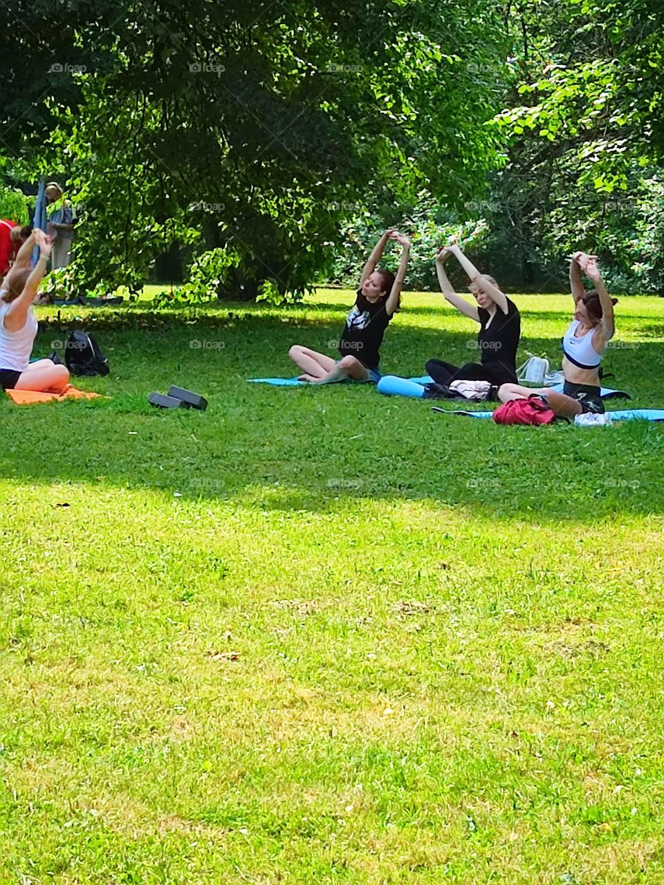 Summer day. Time to bring your body back to normal in the fresh air. Three young girls are sitting on a green meadow and doing yoga. The instructor shows the correct poses