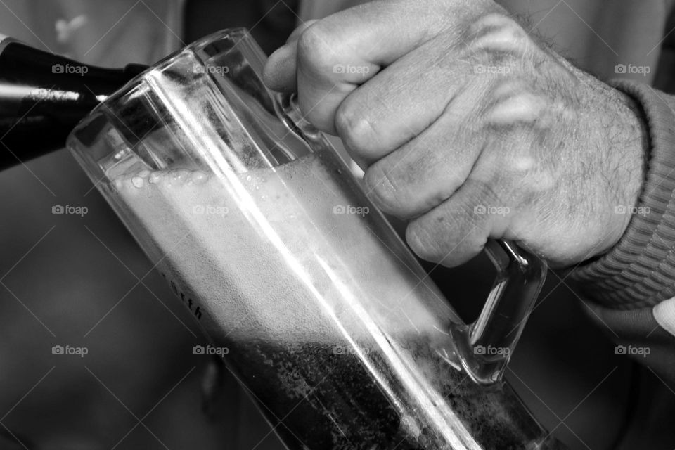 Close-up of a man's hand holding a beer glass and pouring dark beer from a bottle