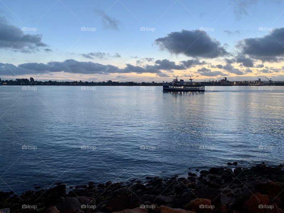 A boat slowly cruises out of the harbor at sunset. 