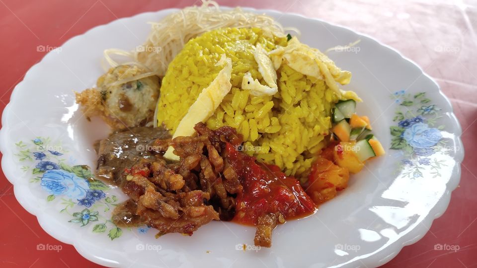 Nasi Kuning, or Nasi Kunyit, popular Indonesian cuisine with coconut milk and turmeric. The rice looks like a pile of gold, often served at parties, as a symbol of good fortune, wealth and dignity.