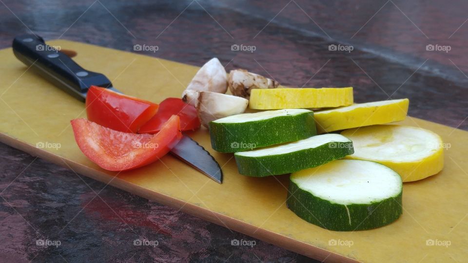 fresh cut vegetables with knife on cutting board cucumbers yellow squash red bell peppers and mushrooms