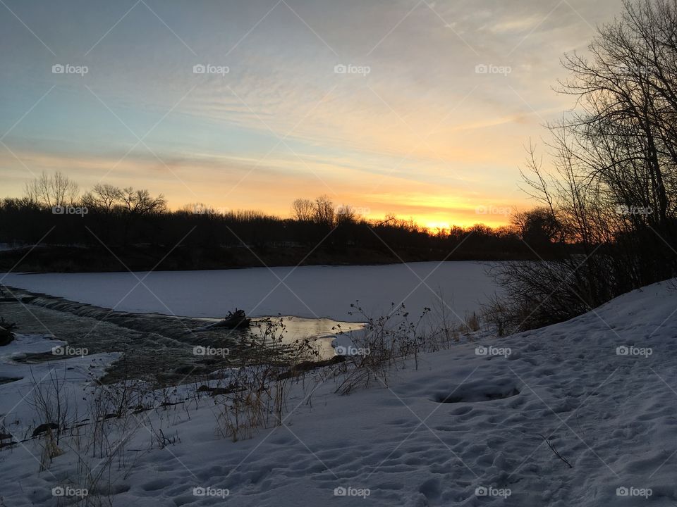 Beautiful winter sunrise over the red river. Flowing water and an orange sky are a gorgeous backdrop to the icy river.