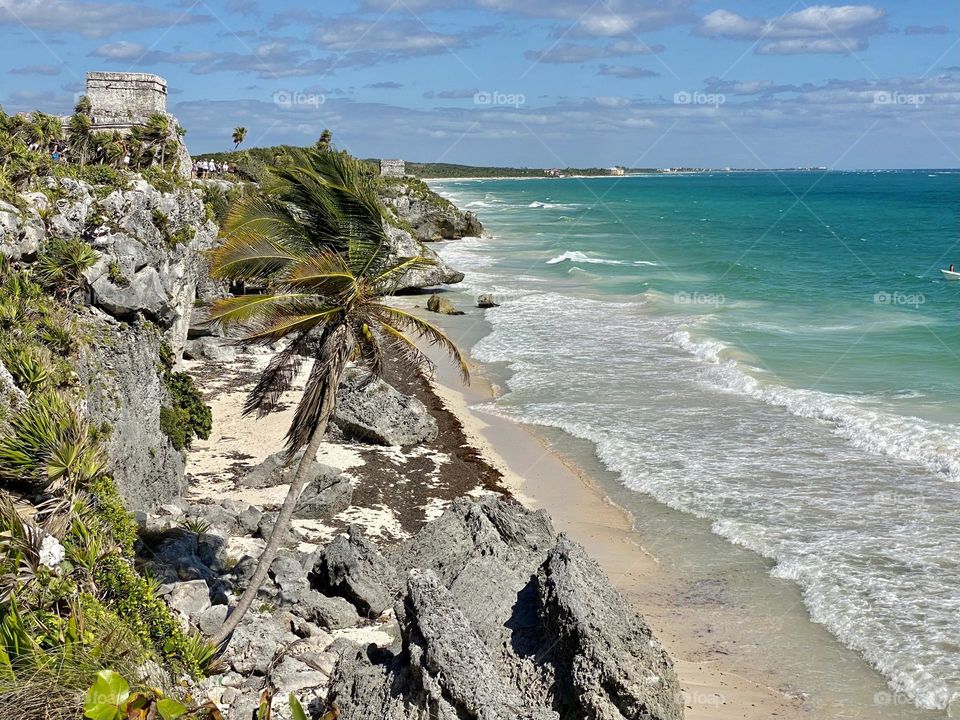 Looking out over the Caribbean from the top of a cliff with a Mayan ruin in the distance 
