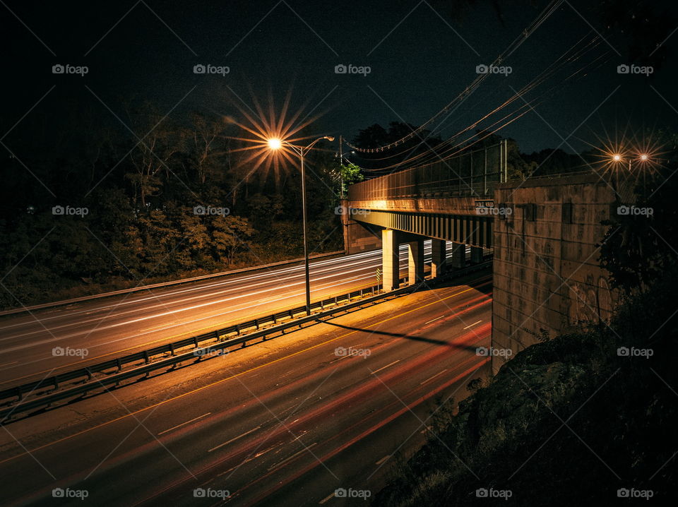 Traffic passing under a bridge taken from on a cliff above the highway at night 