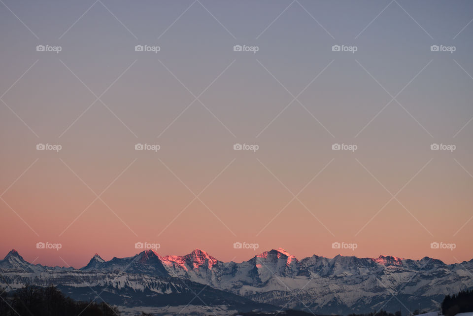 Orange pink glowing light on peaks of mountain range. Colorful gradient in sky.