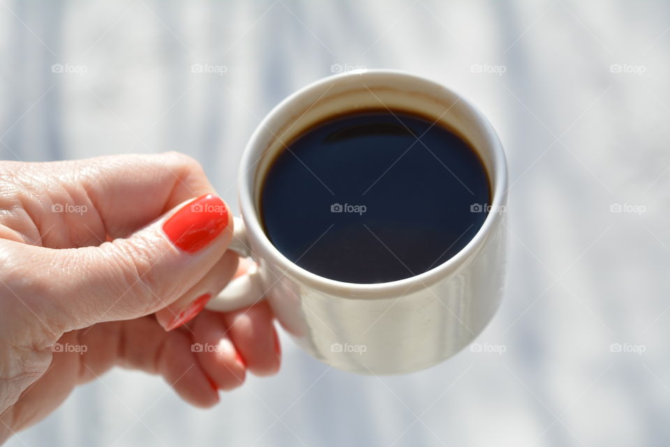 cup of coffee in female hand in sunlight outdoor on a white background, morning routine