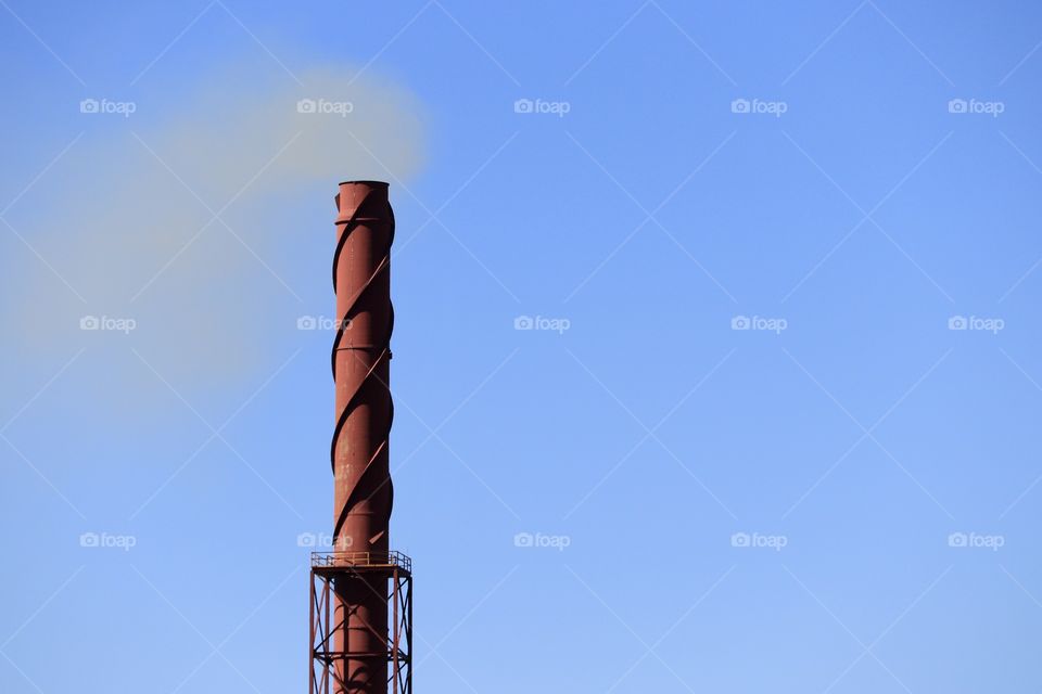 Rusted steel Smoke stack blowing smoke against vivid blue sky minimalism with negative space and room for copy text 