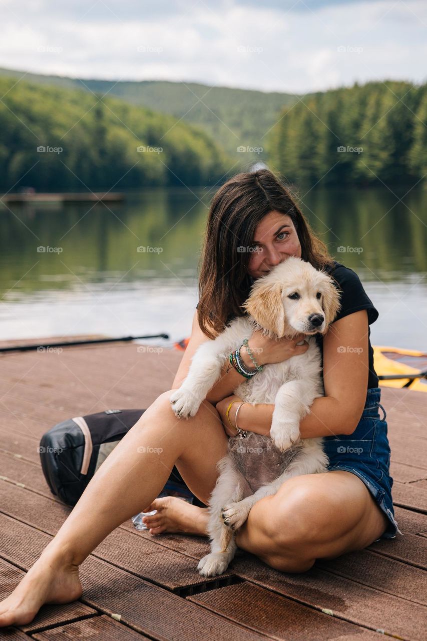 Young woman while being in a vacation in a area with mountains and lakes, showing love for her cute dog.