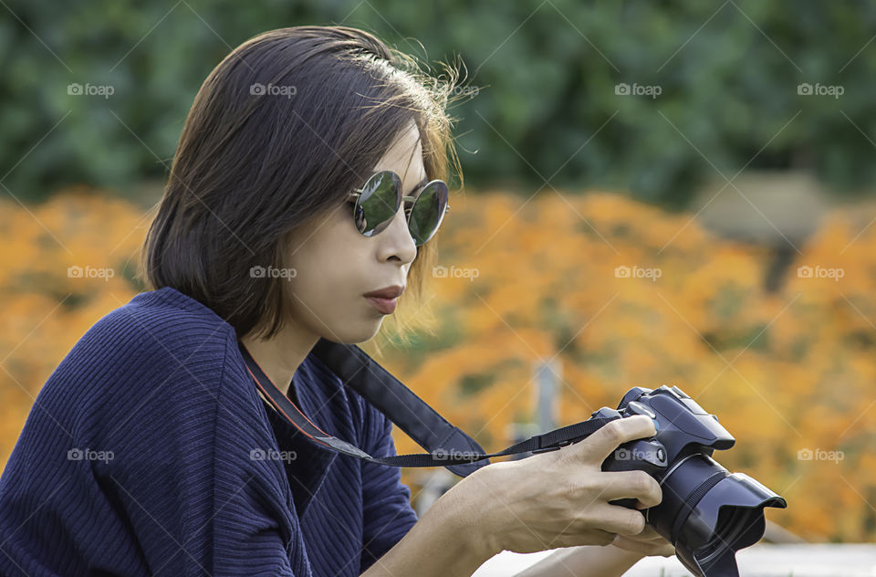 Hand woman holding the camera Background of trees and flowers