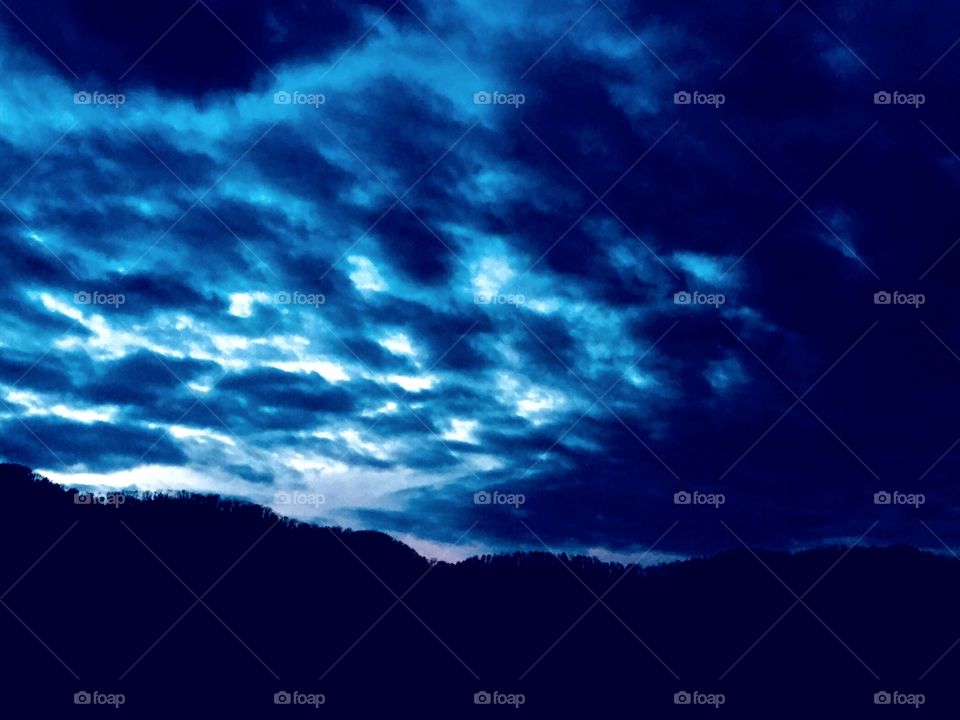Titled...BLUETIFUL...image of rolling black and blue clouds a top a black mountain pillar