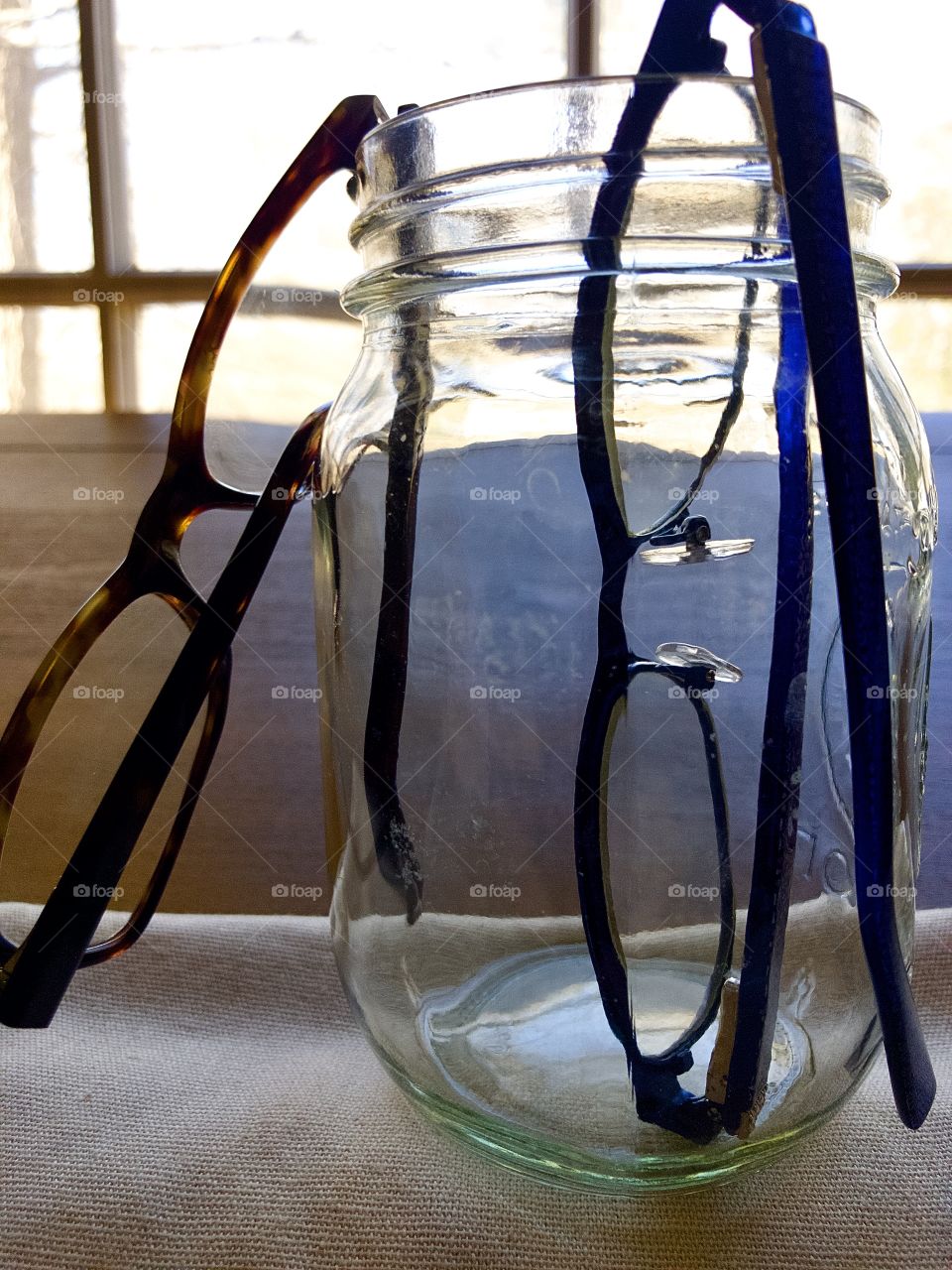 Two pairs of glasses in a glass jar on desk by window 