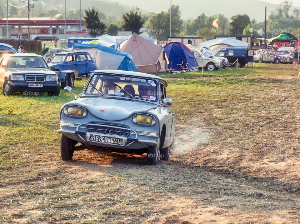 Vintage Citroen oldtimer car driving on a dirt road in a camping place with tents