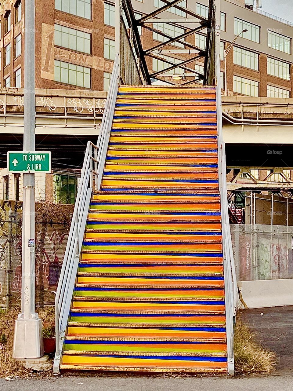 A orange golden staircase is leading up to the pedestrian overpass in Long Island City, Queens, New York that leads to the Van Alst Street and 21st Street MTA G train station. 2021. Hypnotic Productions