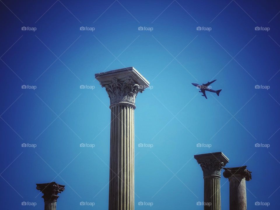 A jet plane flying over ancient Roman columns 