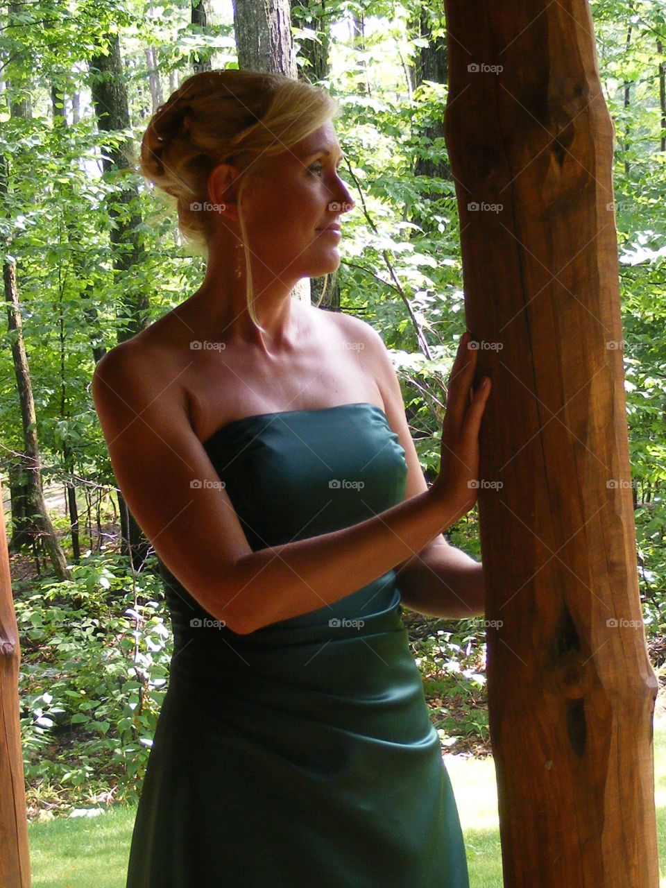 Blond woman in formal gown standing outside a log cabin in the woods