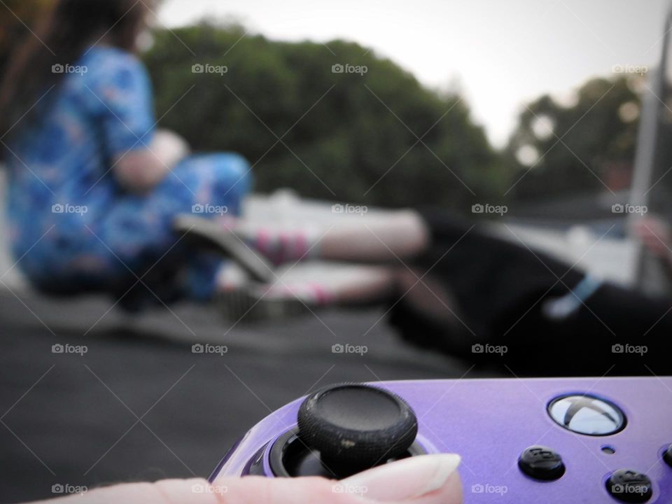 Xbox purple blue colored remote accessory used as if the mother is playing a game called: bring the children on the trampoline and play outside.