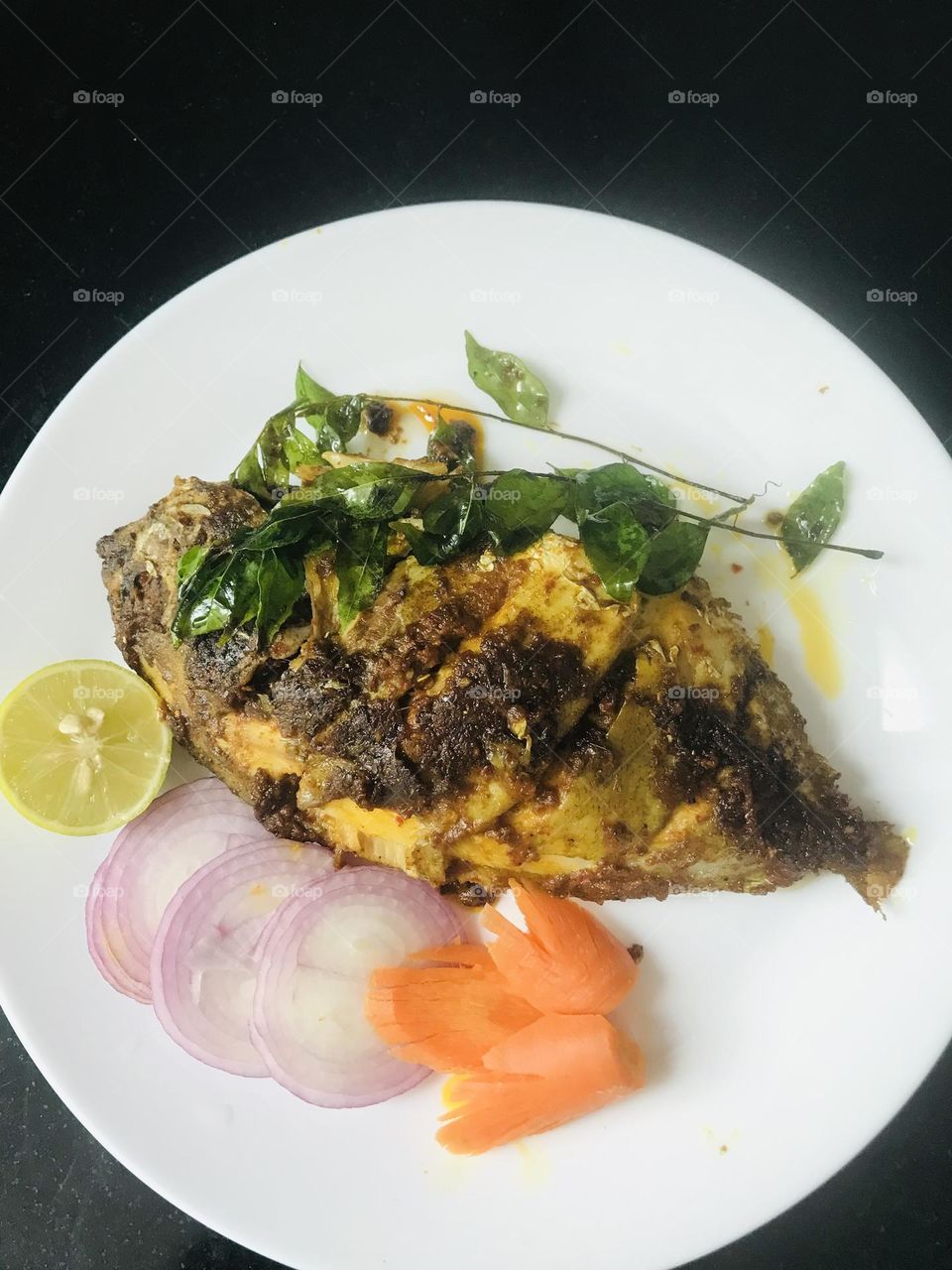 Home made fish fry along with fried curry leaves and sliced onions and carrots and half piece of lemon 