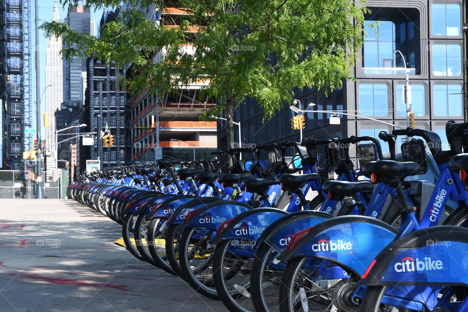 A fleet of blue Citi bikes line the streets and sidewalk on a beautiful day off 10th Avenue in Manhattan.