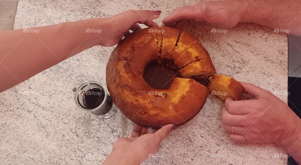 cuatro manos agarrando un bizcochuelo y una sacando un porción y al lado una taza de café