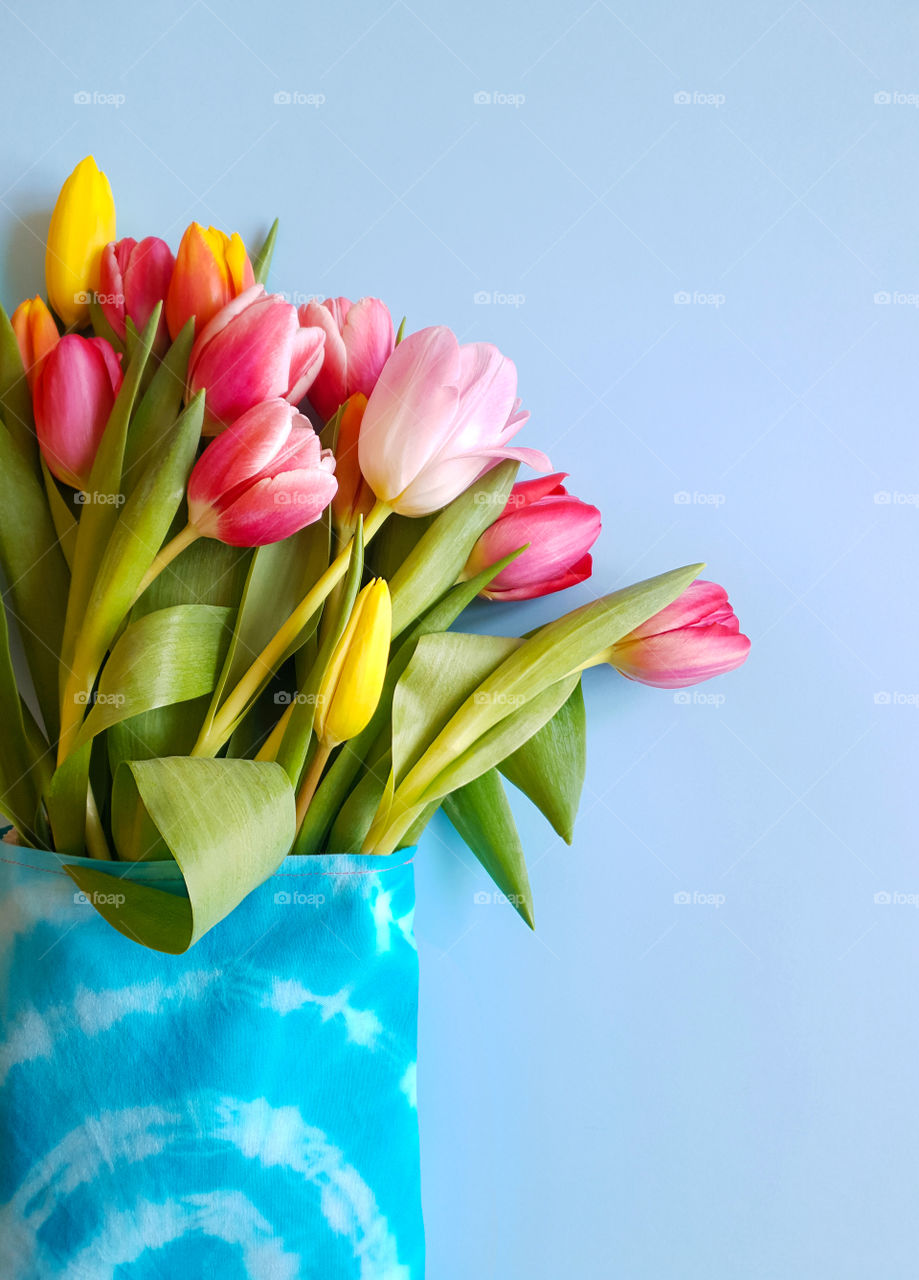 Spring holiday bouquet for Women's Day. Flowers in eco-friendly textile packaging. Concept without plastic. Multi-colored tulips in a woven bag on a blue background. Vertical orientation