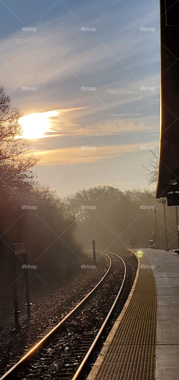Foggy day with sun low in sky, waiting for trains arrival to pick up passengers commuting to South Station in Boston.Tracks disappear around the corner.