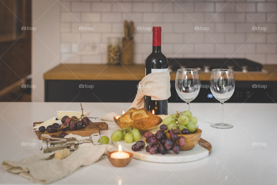 Bottle of red wine on a counter with appetizers, two wine glasses,