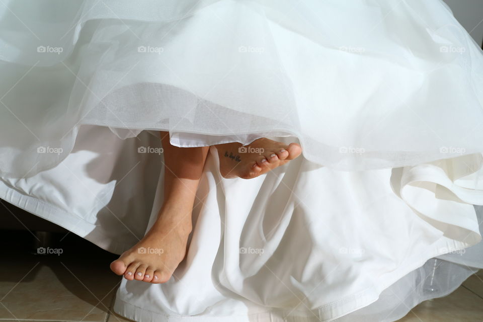 Tatooed Barefoot bride. Bride's feet crossed legs tattooed in script calligraphy under her white dress awaits for groom to arrive