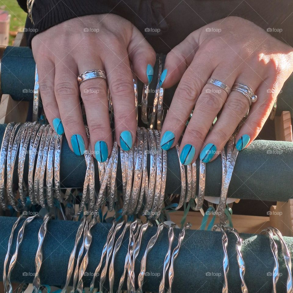Female, pretty hands with turquoise painted nails.Wearing Silver rings. Fingers resting on blue silver bangle display.