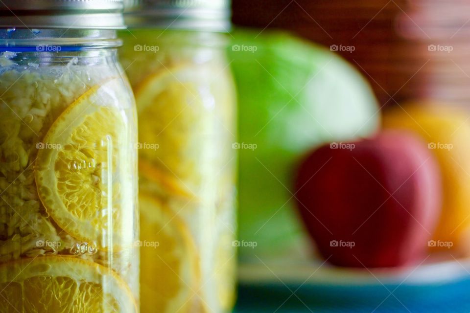 Fermented cabbage, apples and oranges in quart-size mason jars, a cabbage, an apple, and an orange on a white plate on a blue placemat in the background