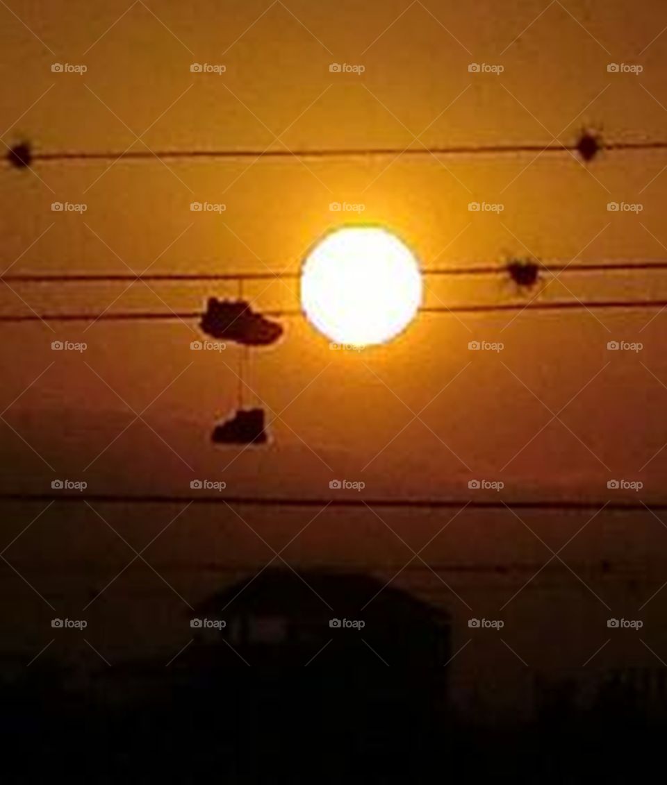 the sunset behind some cables and a pair of shoes hanging