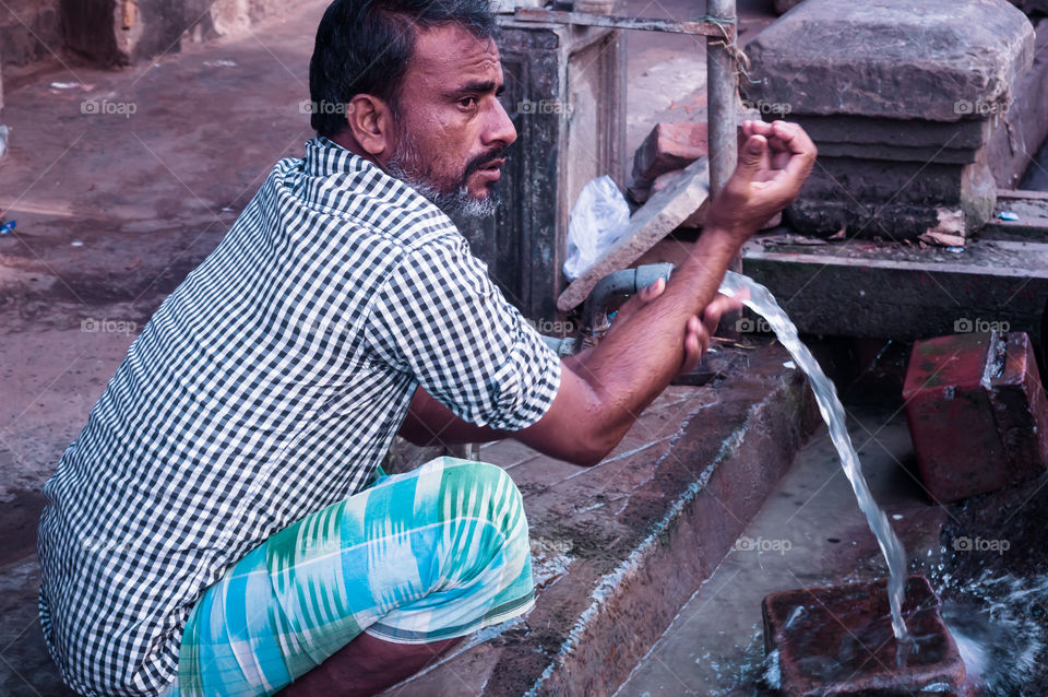 Gandhinagar, Gujrat, India May 2018 - Closeup photo of man washing hands with water from pipe near street road.