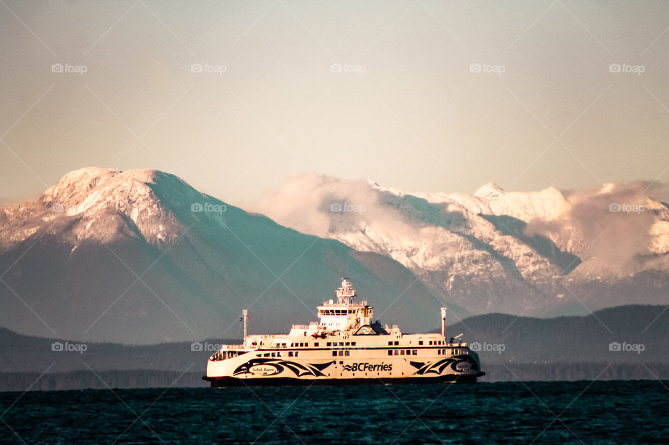 A British Columbia ferry during its crossing between the island & the mainland. Wispy clouds danced between the peaks as the setting winter sun kissed the snow covered mountains & the ferry glowed golden on the deep turquoise blue waters. 